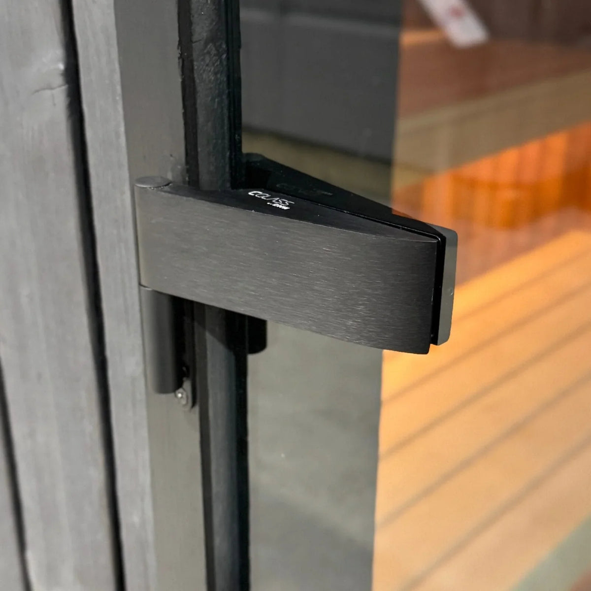 Detail van het donkere scharnier aan de glazen saunadeur